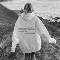 a woman walking down a path with a quote on her hoodie